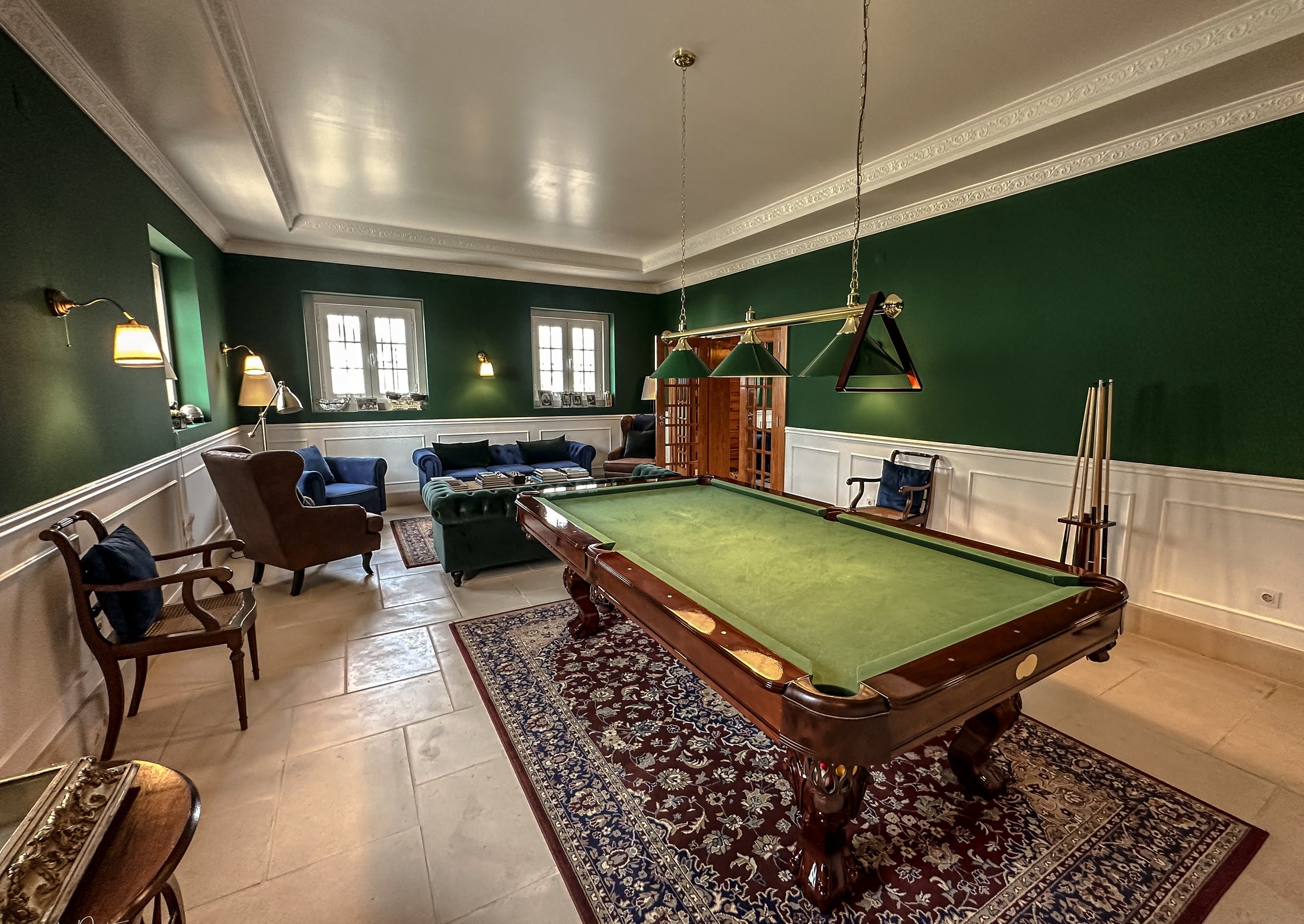 Green games room with billiard table, sofas and brass lamps.