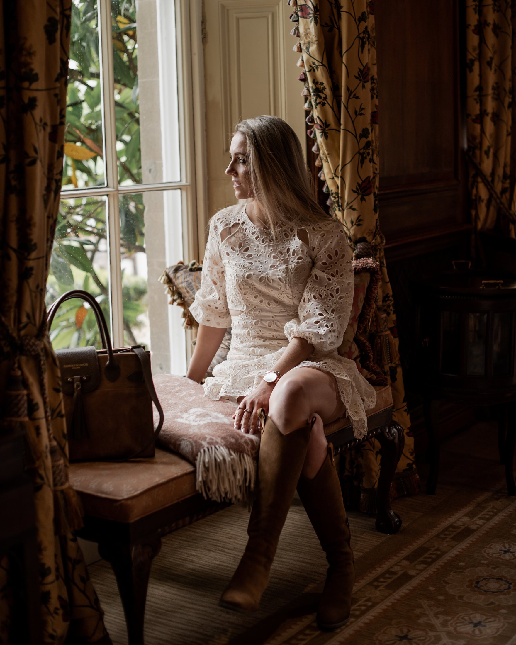 The guest seated on a window seat in a panelled room, morning light.