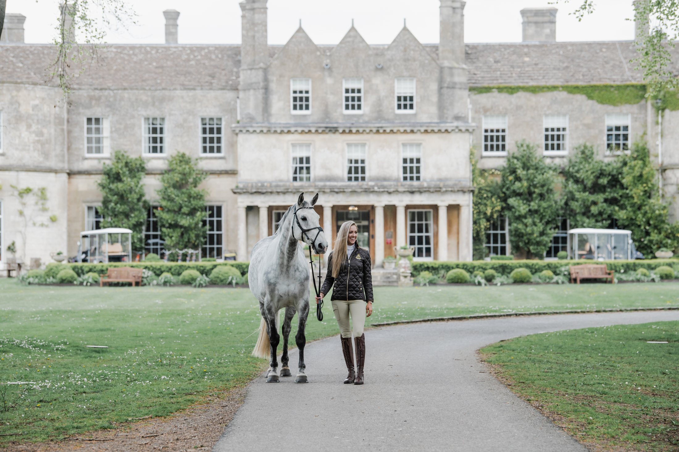 The guest leading a grey horse up the drive, the country house behind.